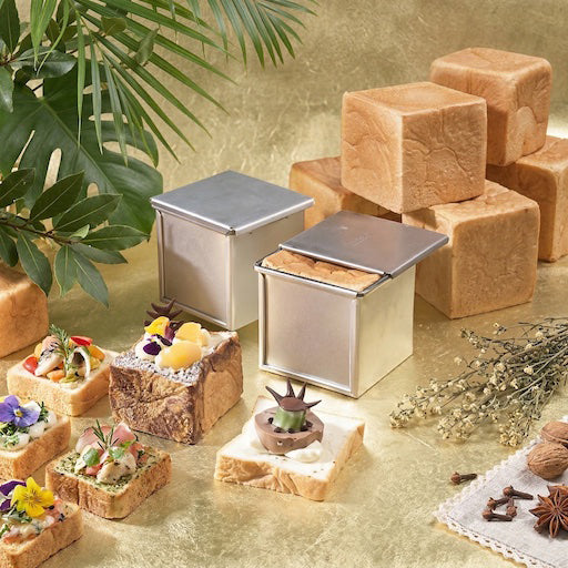 Small square Sanneng cube loaf pans with food on a decorative surface with plants and flowers.