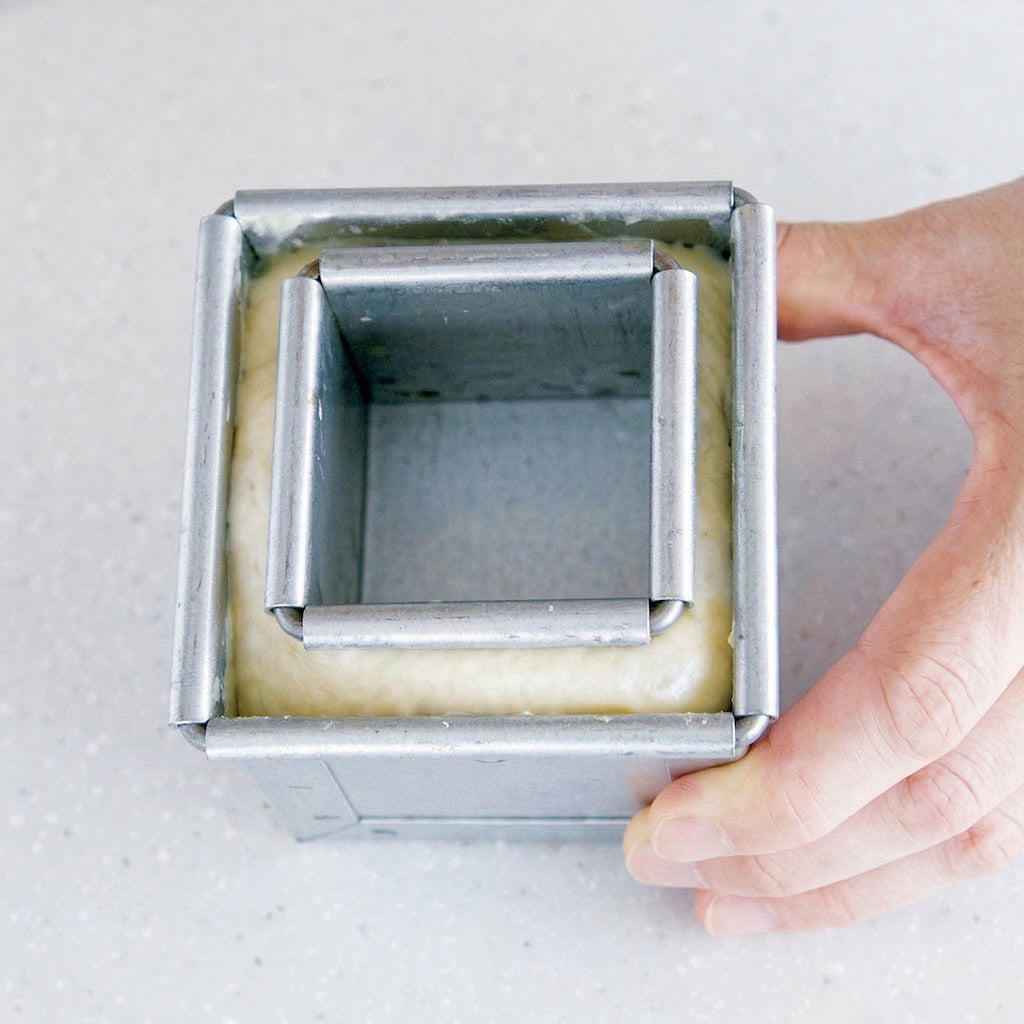 Aluminum Sanneng square cake pan held by a hand on a light gray background