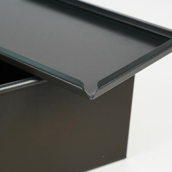 Close-up of a black metal lid corner of Sanneng loaf pan on a white background