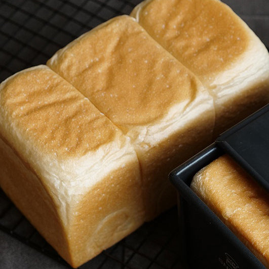 Loaf of bread in a Sanneng black non-stick loaf pan on a dark surface