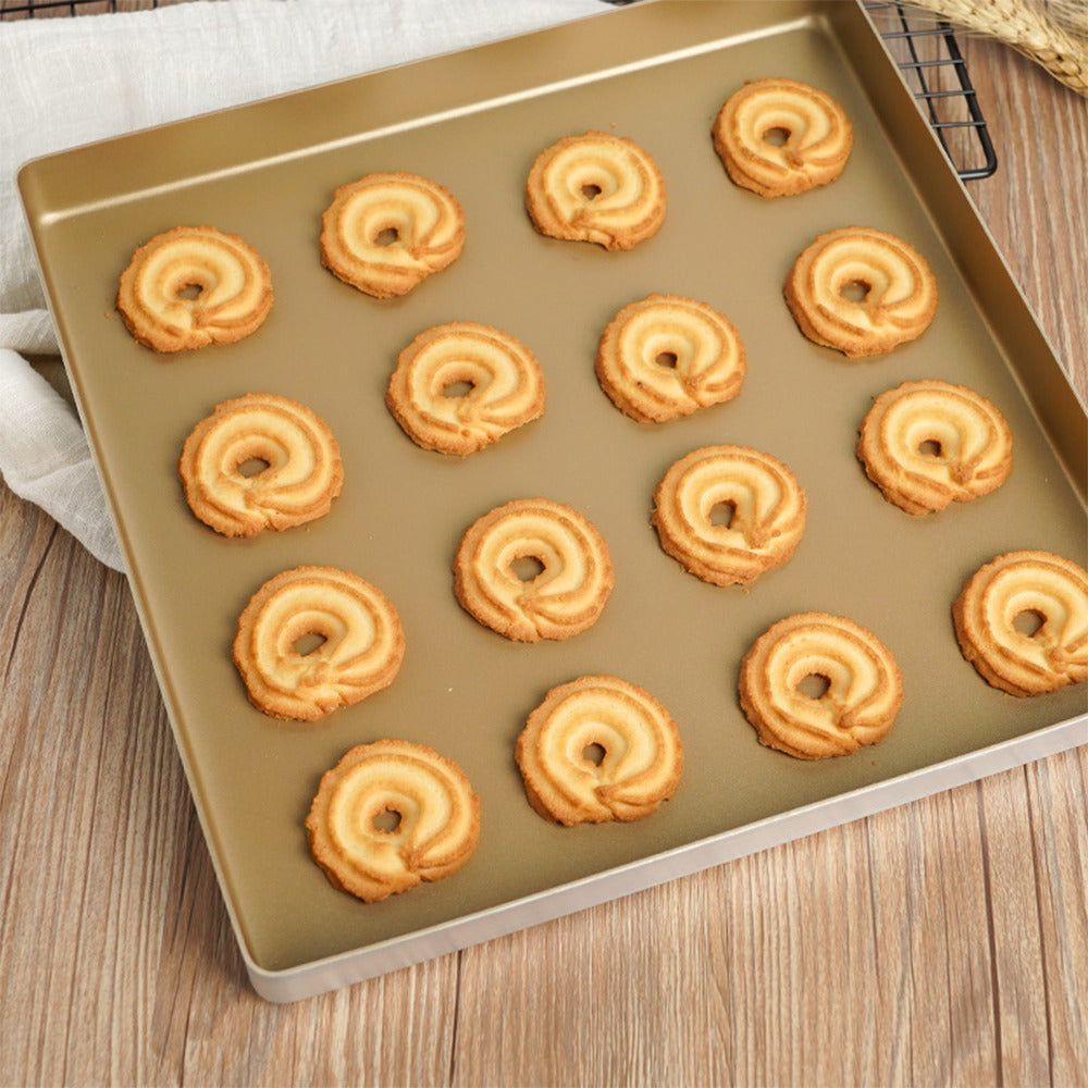 A square Sanneng non-stick baking pan filled with 15 swirled ring-shaped cookies, photographed from above on a wooden surface with a light fabric and cooling rack partially visible.