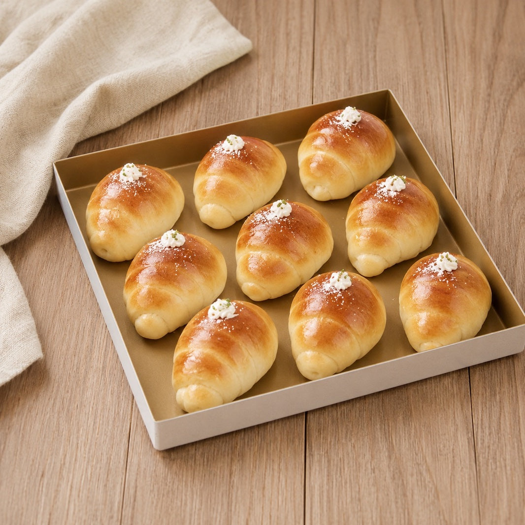 Nine golden-brown asian roll pastries topped with white crumb, arranged in a square Sanneng baking tray on a light wood surface with a beige cloth in the corner.