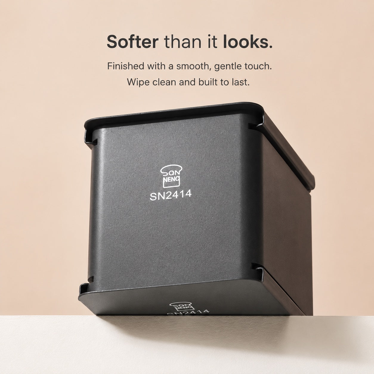 Sanneng matte black square wall-mounted dispenser or container with a lid, shown on a light beige background with promotional text above. The product has visible branding and model text on the front.