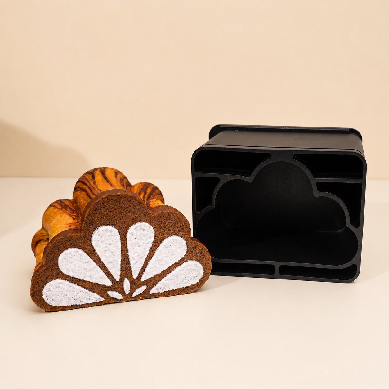 A cloud-shaped Shokupan bread with brown and white patterned fabric and orange tiger-print inner layers, shown next to Sanneng black non-stick cloud-shaped toast box pan on a beige background.