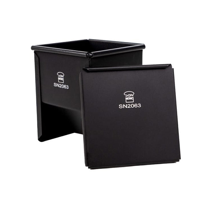 A black metal rectangular Sanneng baking pan with lid, shown open with the lid leaning in front. The container has a white printed logo and the text 'SN2063' on both the side and the lid.