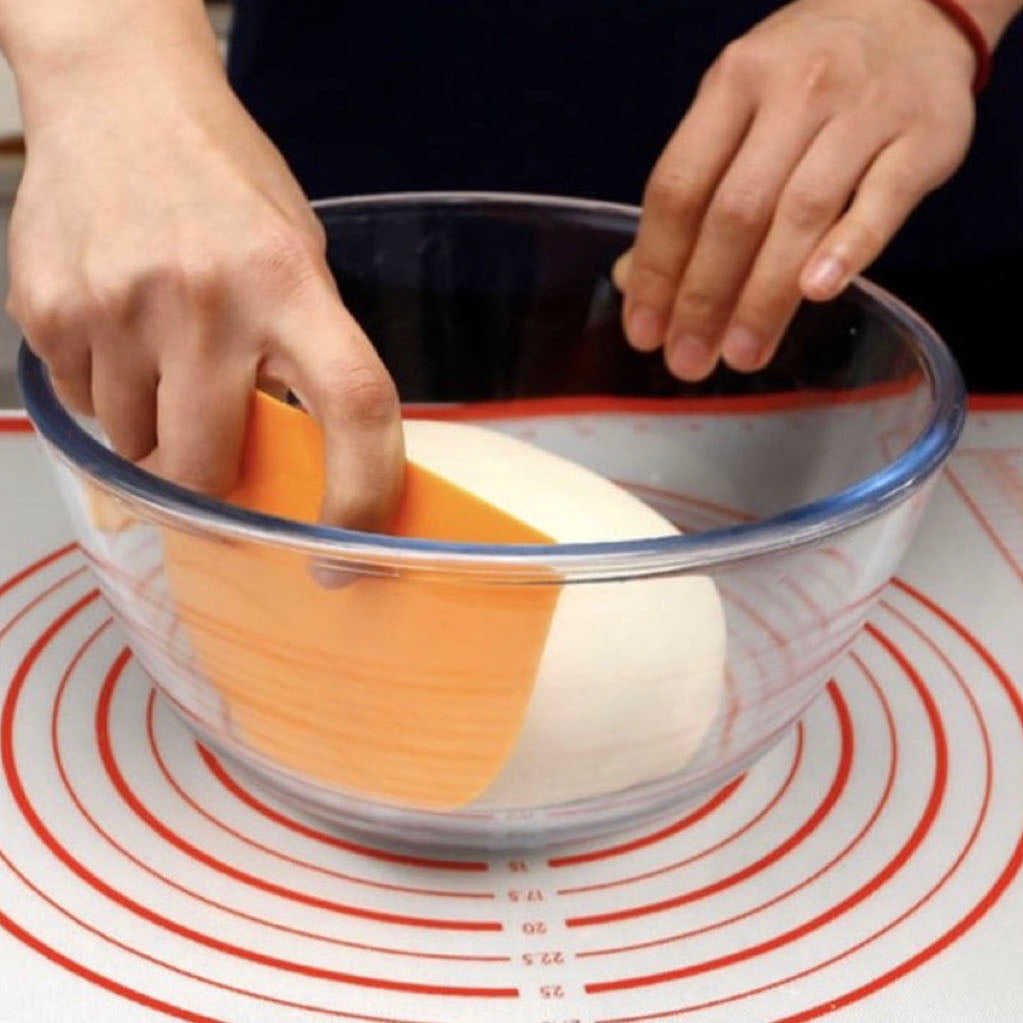 Person using a yellow SN4073 Sanneng scraper to clean a glass bowl on a red and white circular mat.