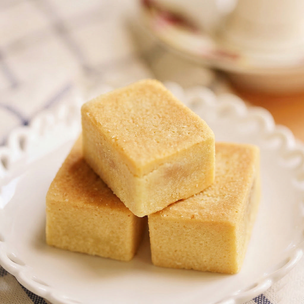 Three square pieces of yellow pineapple cake on a white plate with a blurred background
