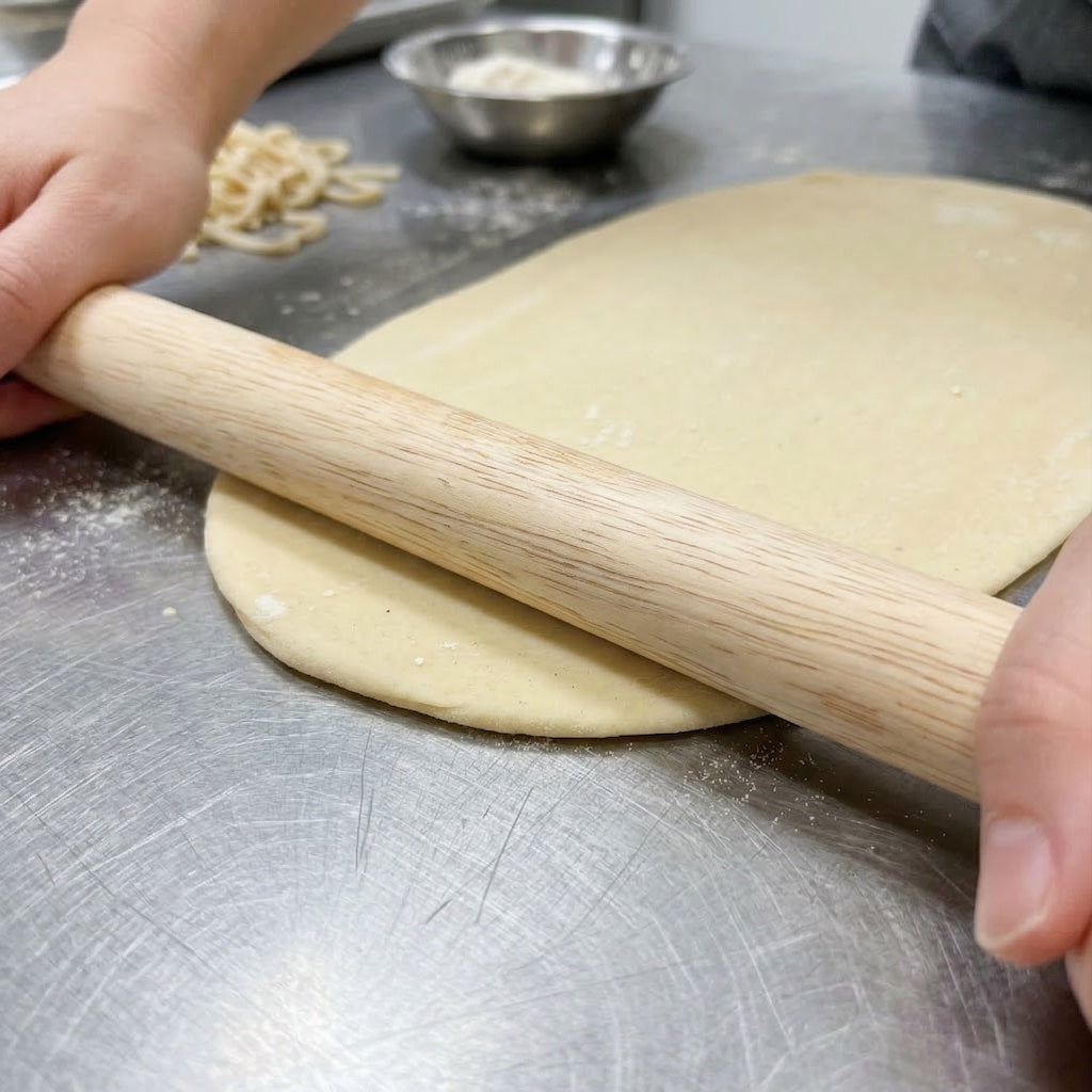 Person rolling dough with a Sanneng Small Wooden Rolling Pin SN8030 on a metal surface.