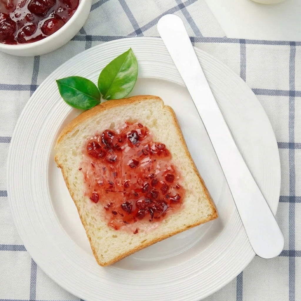 Toast with red jelly on a white plate with a Sanneng stainless steel multi-purpose spatula SN4061, on a checkered tablecloth.