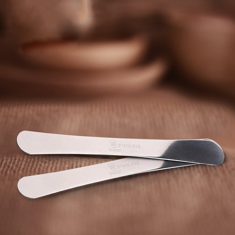Two metal SN4061 Sanneng spatulas on a brown surface with a blurred background