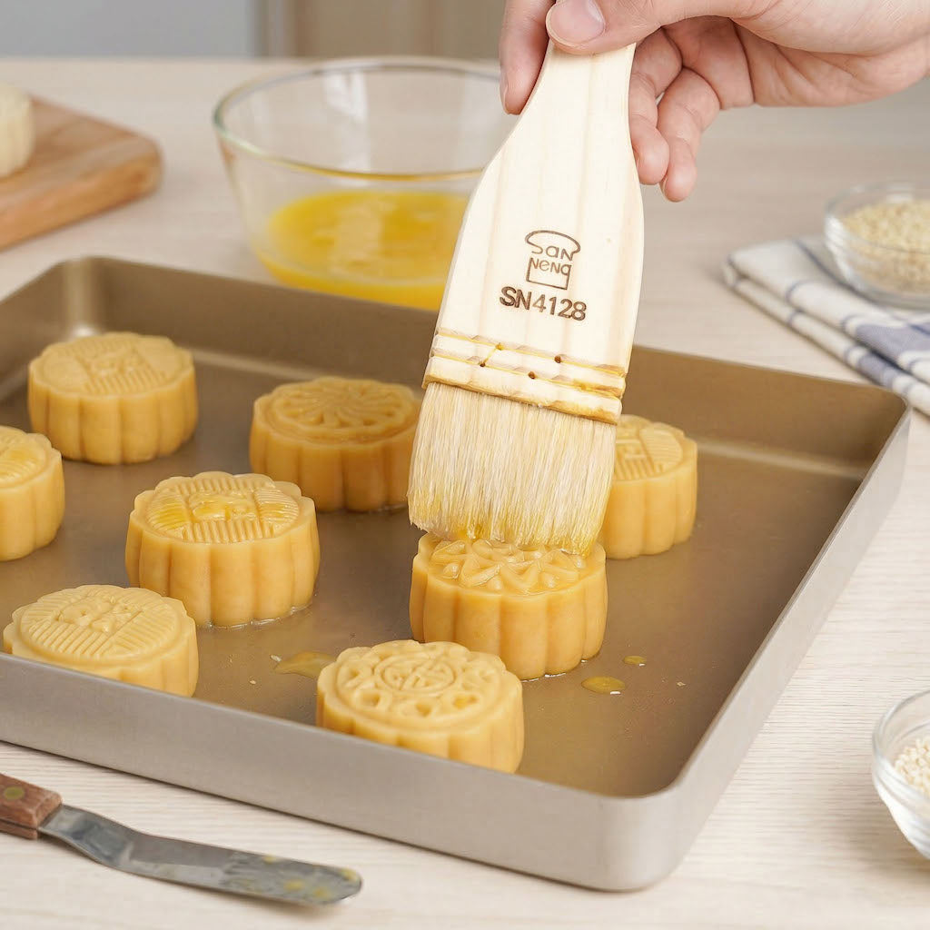 Person brushing mooncakes with a Sanneng wooden pastry brush on a baking tray
