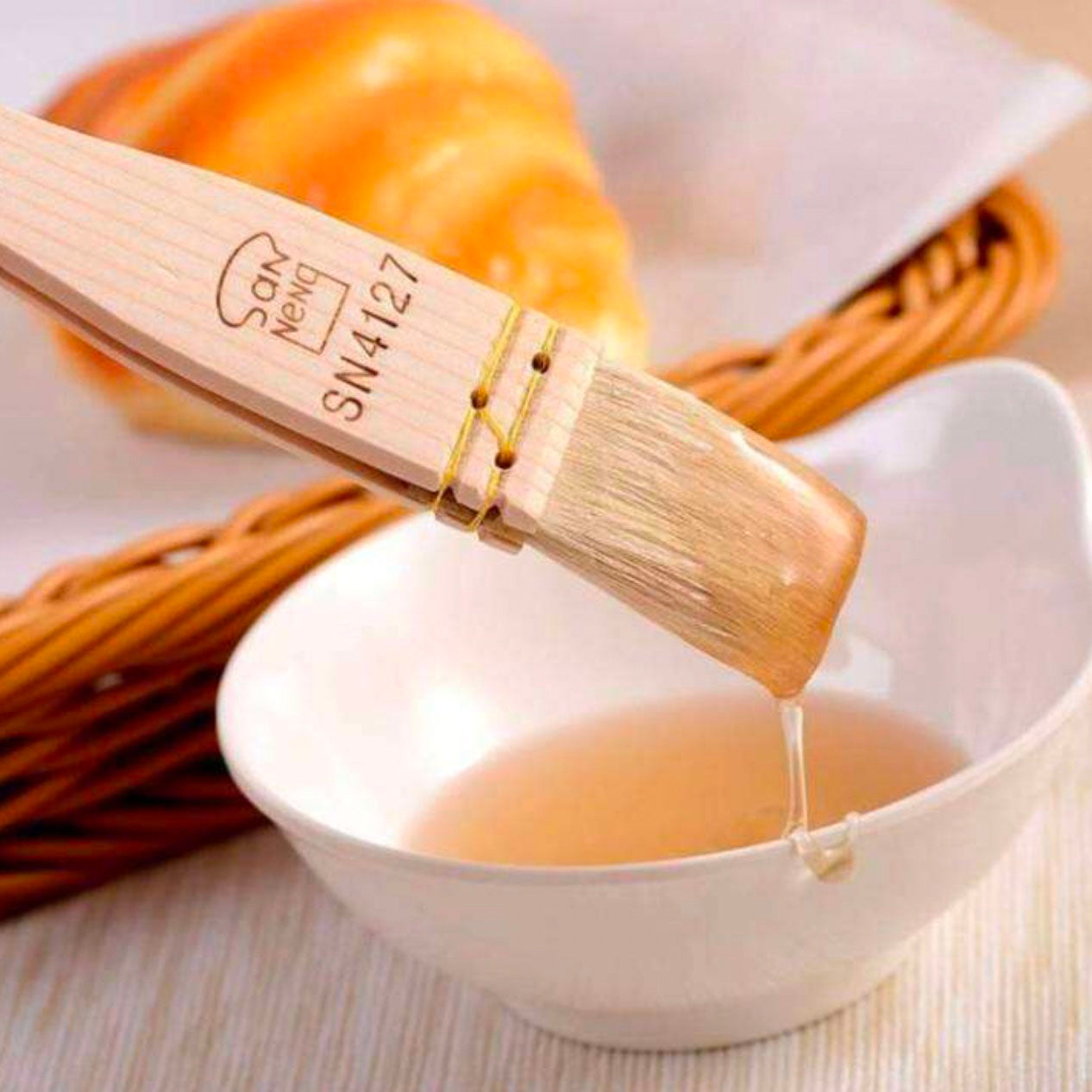 Wooden Sanneng pastry brush with engravings being used to pour a liquid into a white bowl.