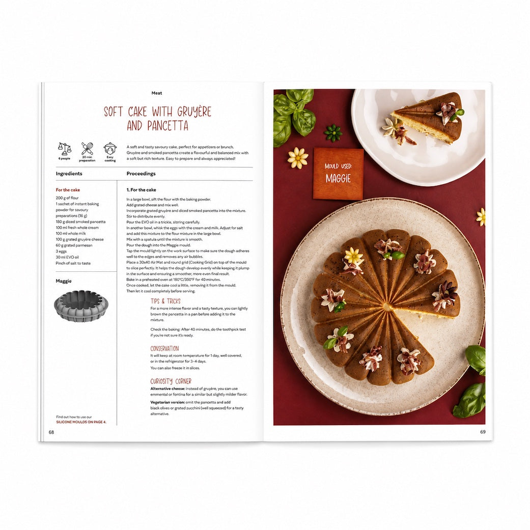 An open Silikomart recipe book showing a recipe for soft cake with crèsbe and pancetta. The left page contains ingredients, instructions, and a pie mold diagram, while the right page features a styled food photograph of a sliced and whole cake decorated with small flowers, set on a dark red surface with basil leaves.