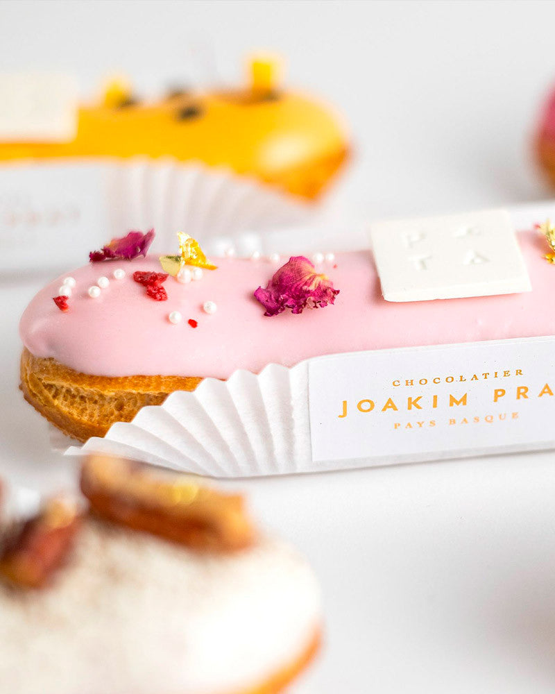Pastry with pink icing and dried flowers, branded 'Joaquin Prat', on a white background