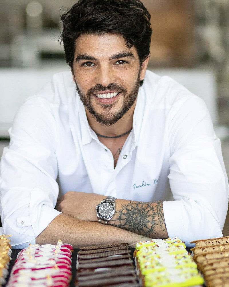 Joakim Prat in a white shirt, standing in front of a display of pastries.