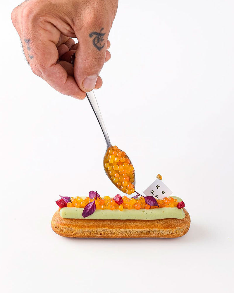 Hand with a spoon adding caviar to an eclair on a white background