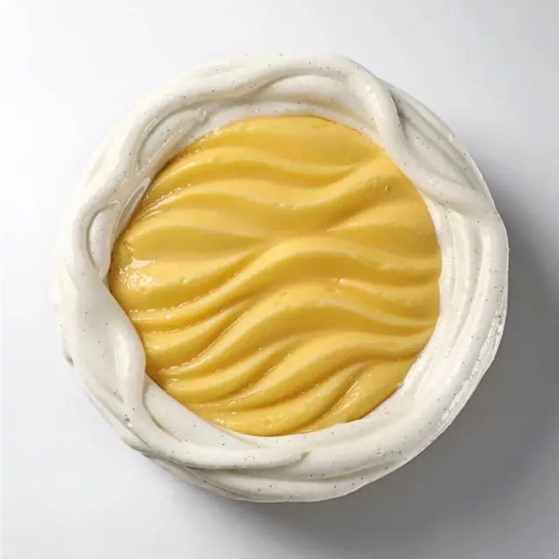Bowl of yellow frozen dessert with white cream on a light gray background