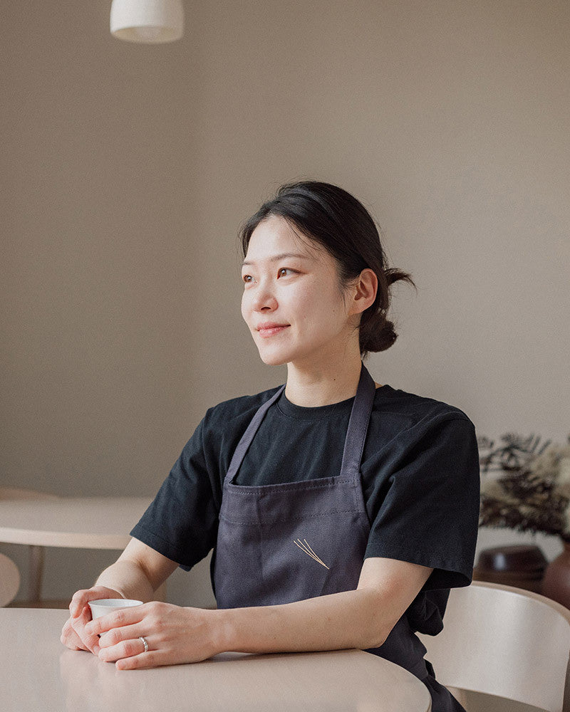 Chef wearing a dark apron sitting in a room with a neutral background