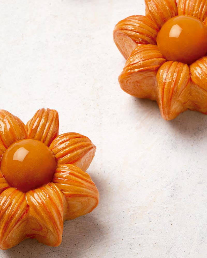 Two orange flower-shaped croissaint ties on a light gray background