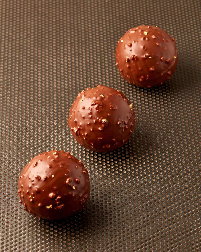 Three chocolate truffles with a textured surface on a brown textured background