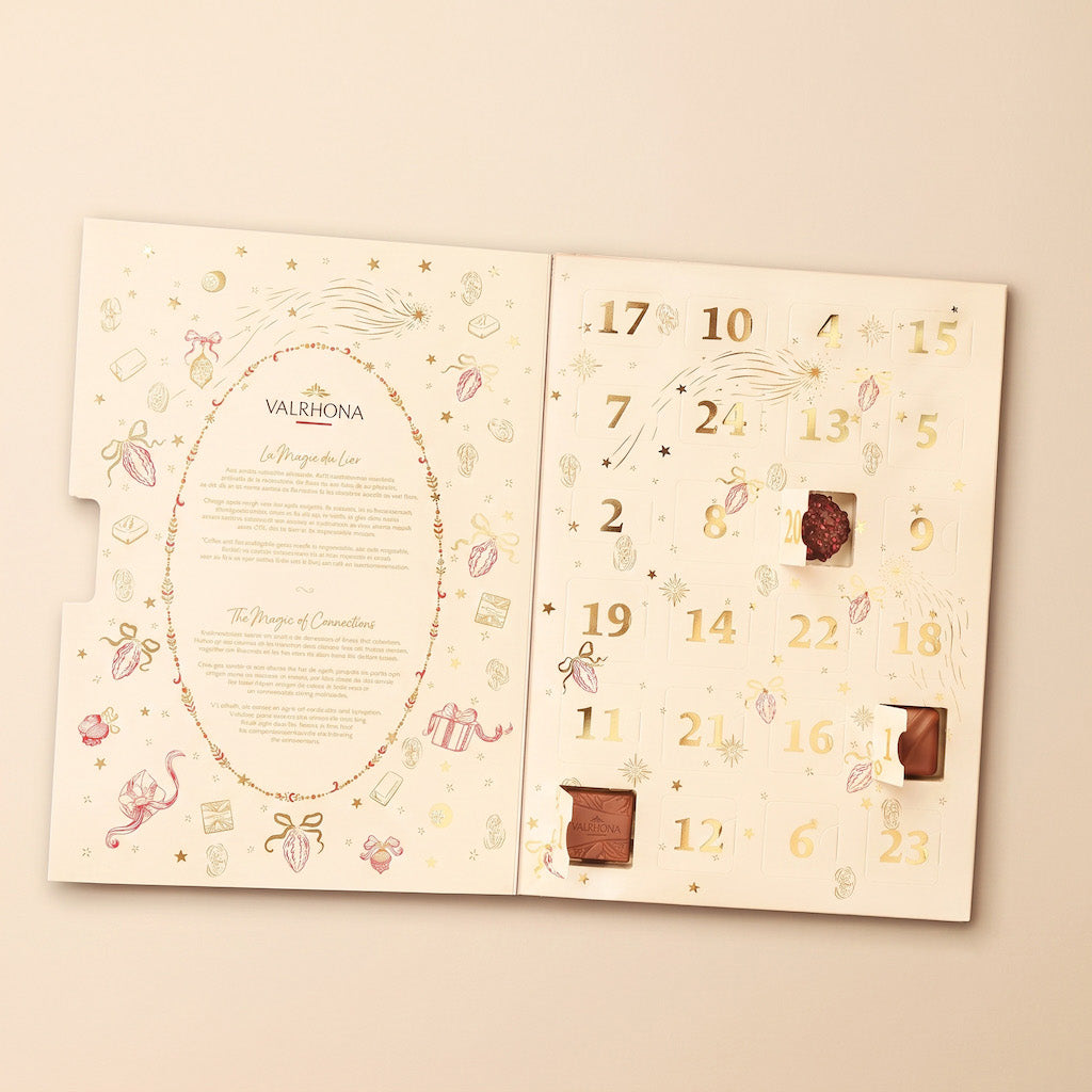 An open Valhina chocolate advent calendar on a light beige background. The left page features elegant gold and pink illustrations with the brand name 'VALHINA' and event text.
