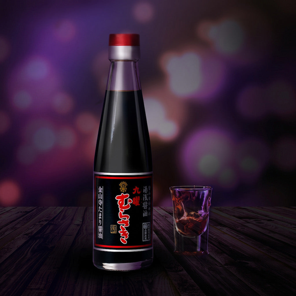 A bottle of Yuasa Kuyo Murasaki Soy Sauce with a black label and red cap sits on a dark wooden table next to a small clear drinking glass, against a blurred purple bokeh background.